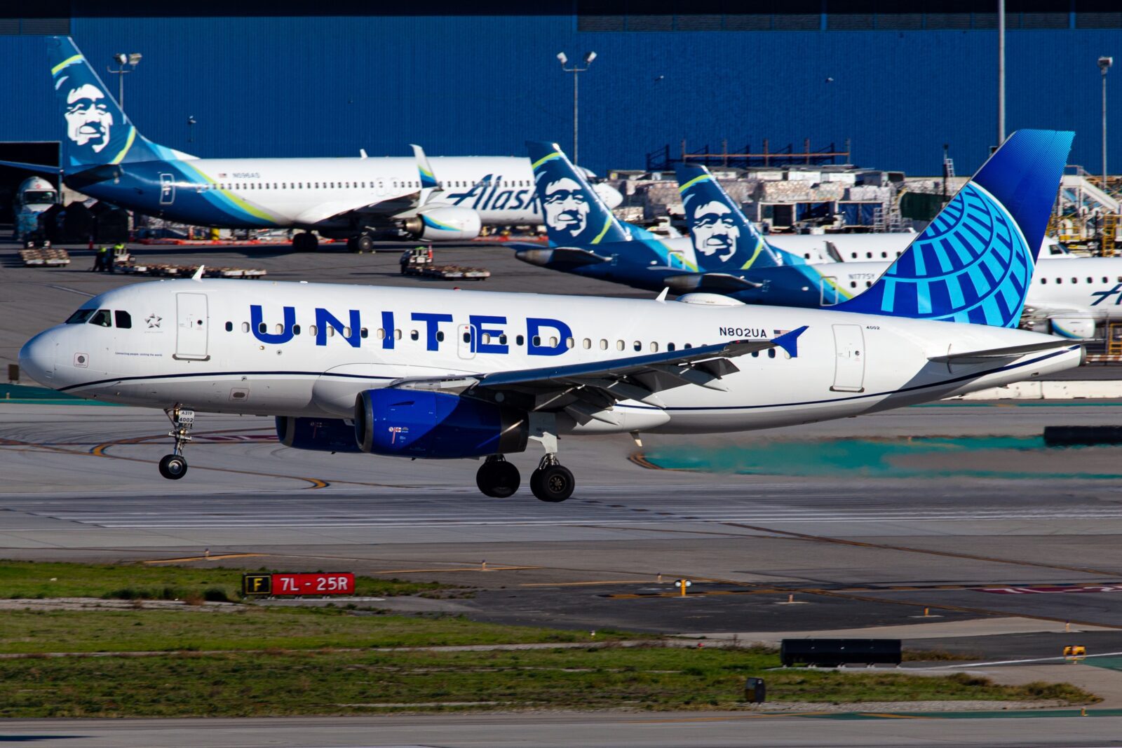 A united airlines airbus a319 landing in front of several Alaska Airlines airplanes